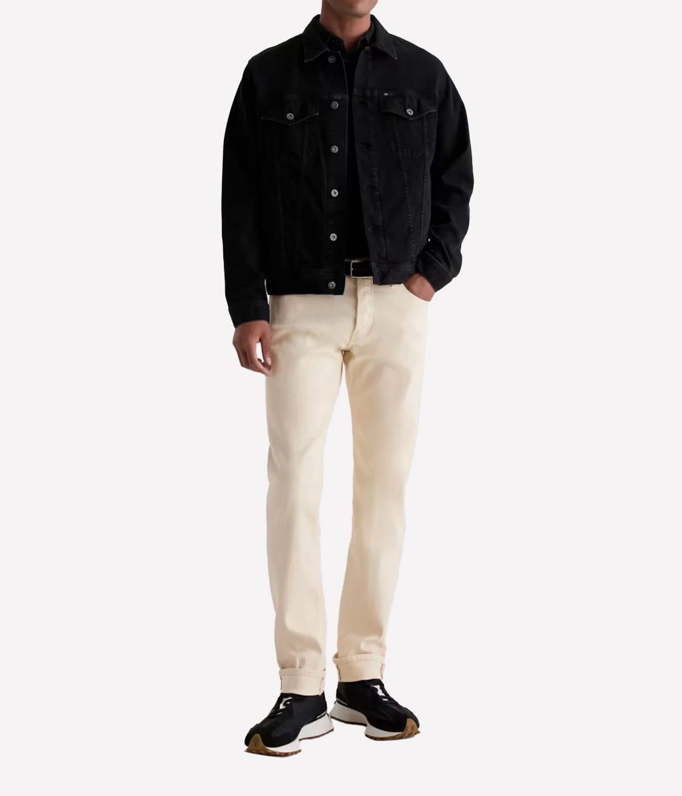A model wearing a black denim jacket, off-white slim-fit jeans, and black sneakers, standing against a plain light gray studio background.