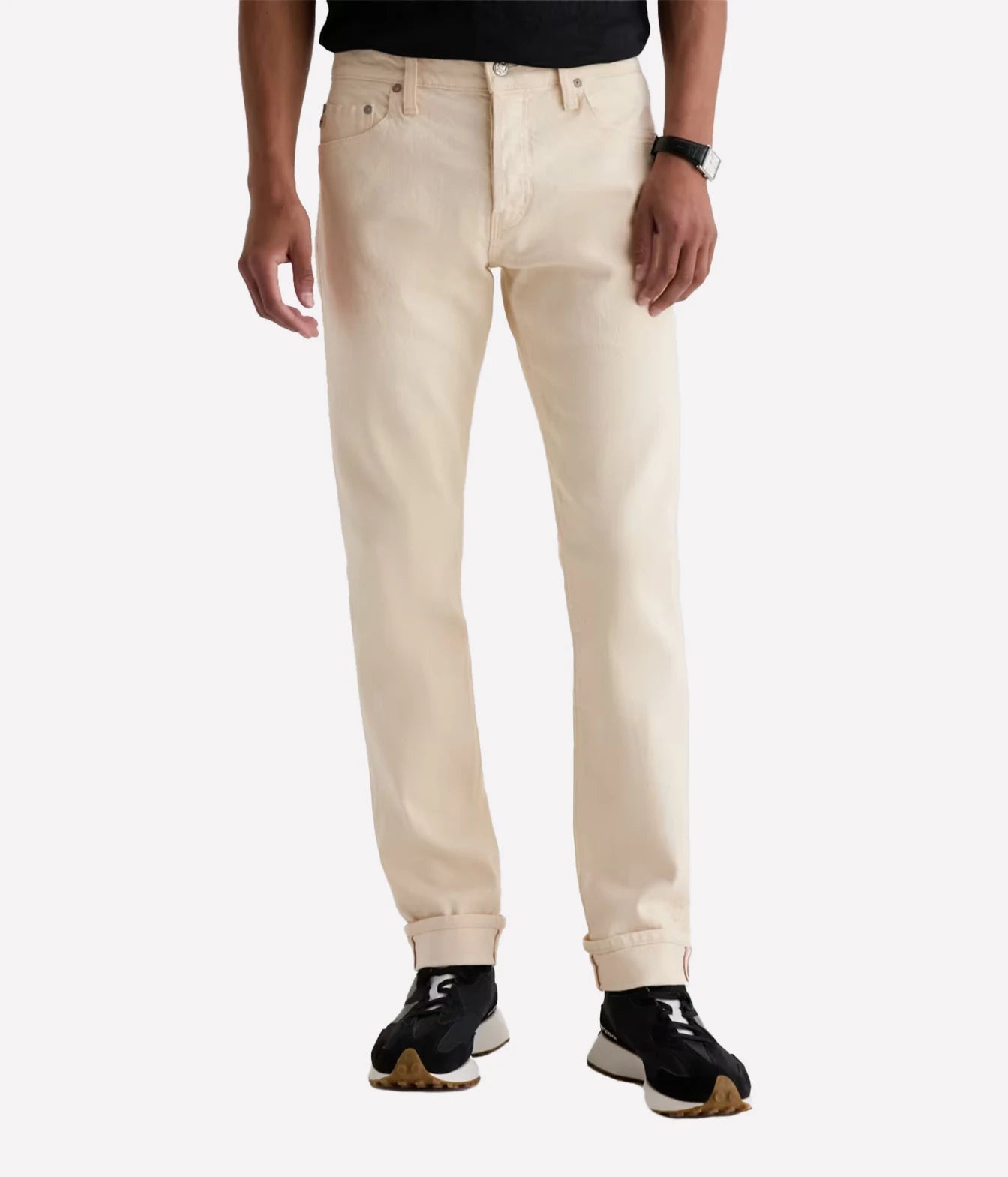 A person wearing light cream-colored slim-fit jeans with rolled cuffs, paired with black sneakers and a black top, shown from the waist down on a light gray background.