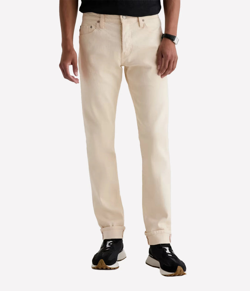A person wearing light cream-colored slim-fit jeans with rolled cuffs, paired with black sneakers and a black top, shown from the waist down on a light gray background.
