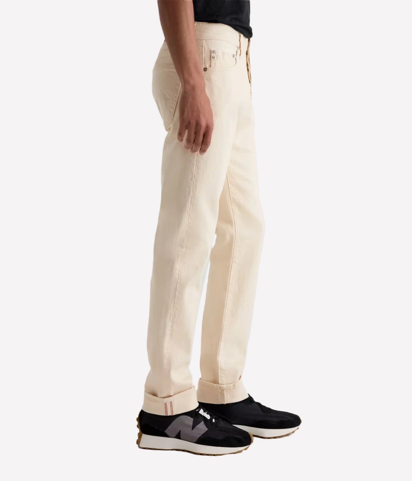A side profile view of a person wearing off-white denim jeans and black New Balance sneakers against a plain white background.