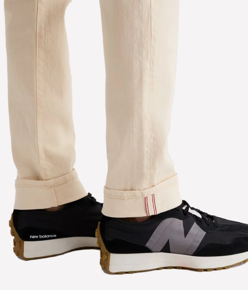 Close-up of a person's legs wearing off-white cuffed jeans and black New Balance sneakers with a gray 'N' logo and brown gum outsole, against a plain white background.