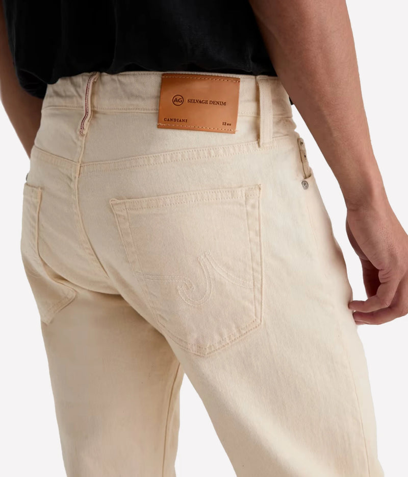 Close-up back view of a person wearing light cream denim jeans, showing the waistband, leather brand patch, back pocket, and hand at the side against a plain light background.