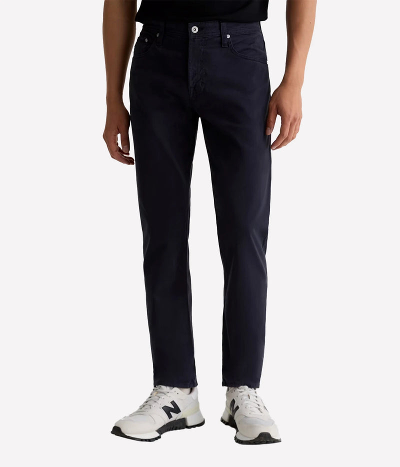 A person wearing dark navy slim-fit jeans with white New Balance sneakers, shown from the waist down on a light gray studio background.