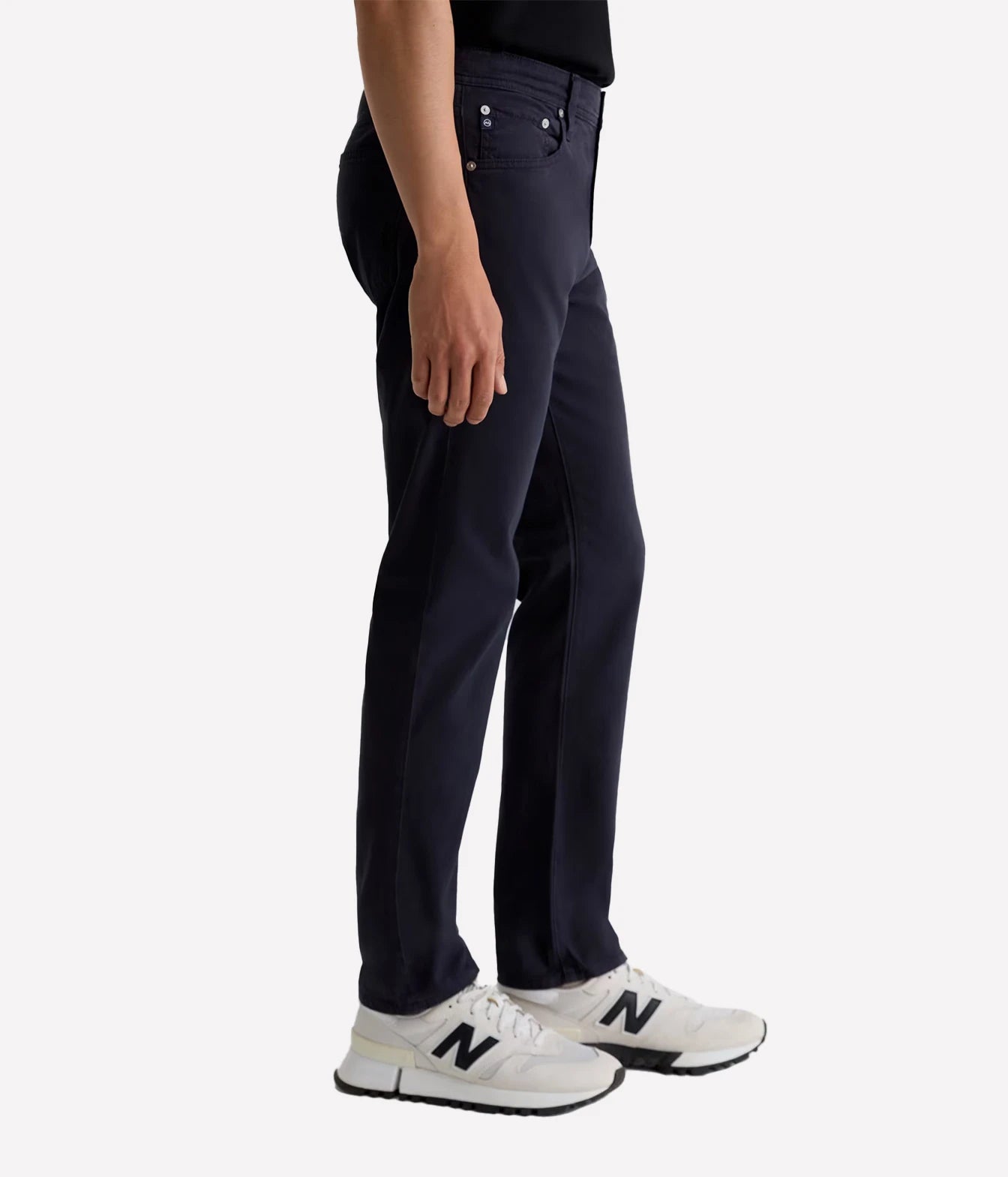 A side-profile view of a person wearing dark navy blue pants and white New Balance sneakers against a clean white background.