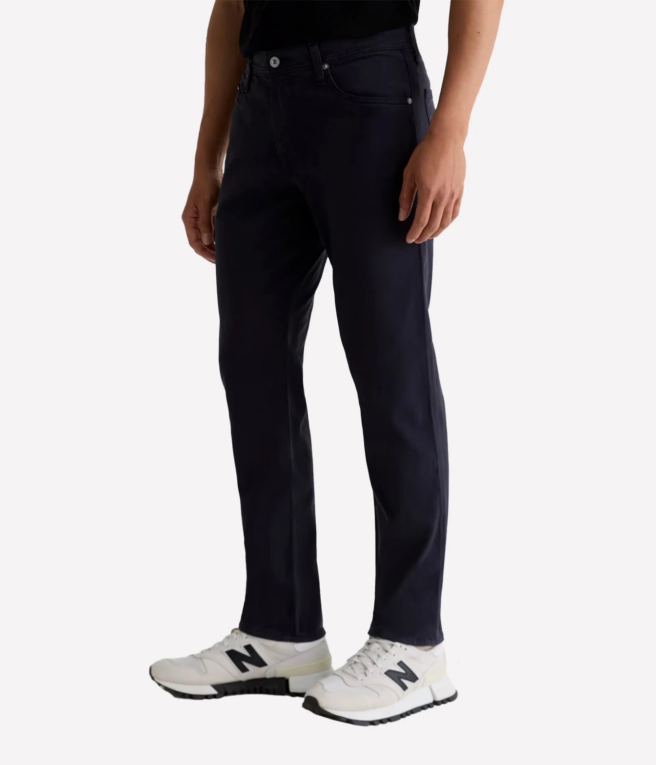 A person wearing dark navy slim-fit jeans and white New Balance sneakers, shown from the waist down against a light gray studio background.