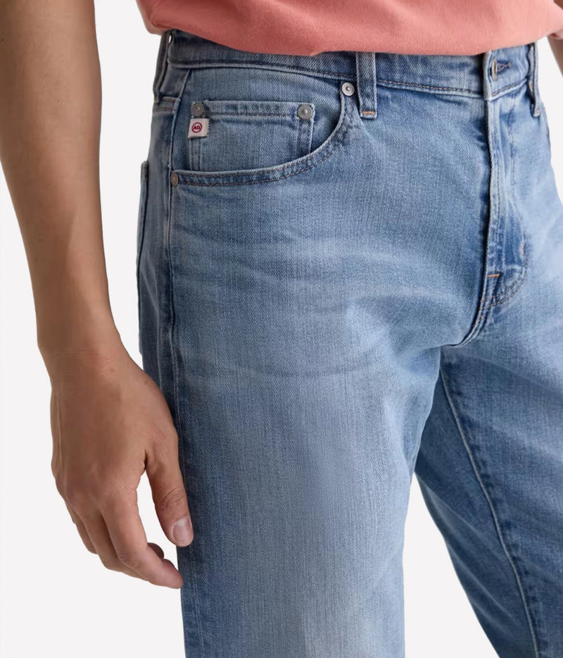 Close-up of a person wearing light blue denim jeans, showing the back pocket and waistband area against a plain light background.