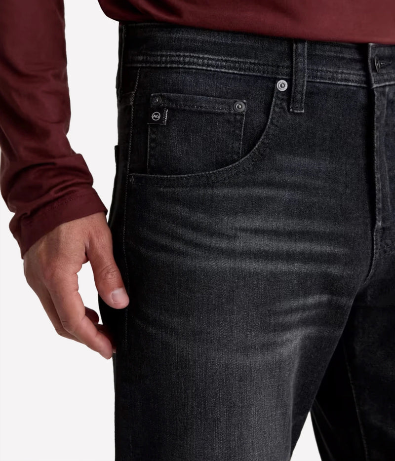 Close-up of a person wearing dark washed denim jeans with a maroon long-sleeve shirt, showing the front pocket and waistband details against a light gray background.