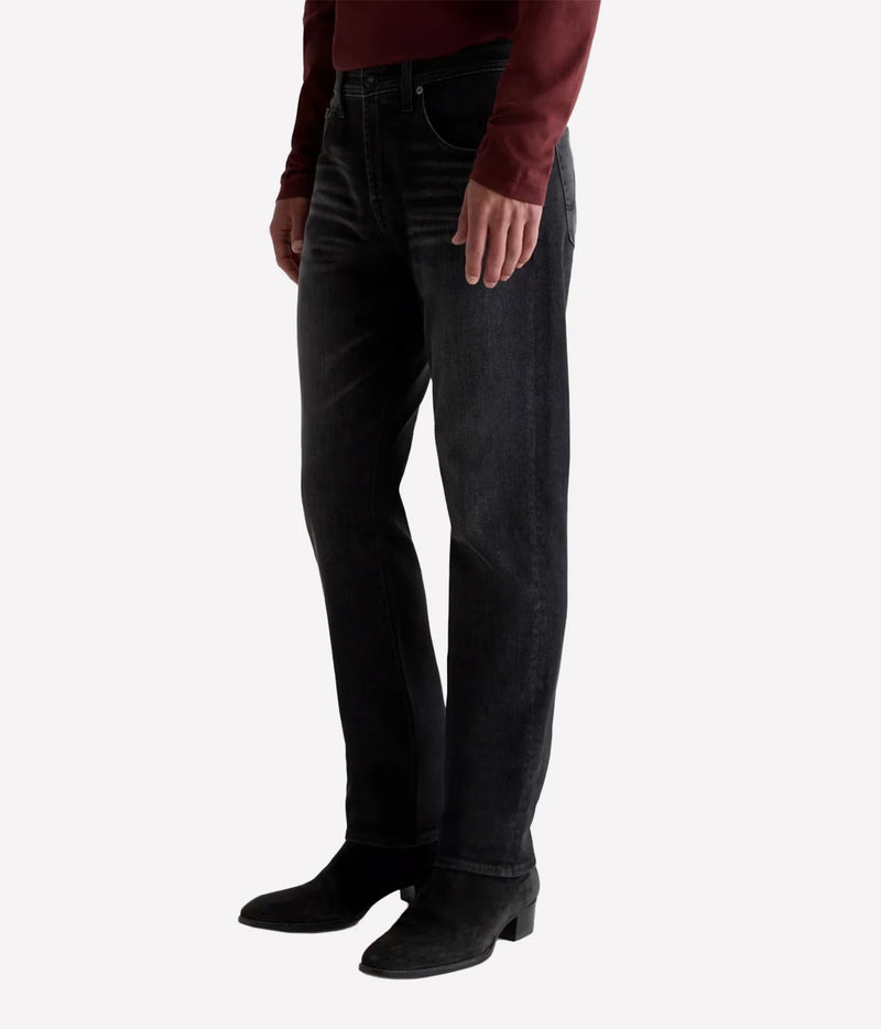 A person wearing dark charcoal-wash straight-leg jeans, a burgundy long-sleeve top, and black ankle boots, shown from the waist down against a light gray studio background.