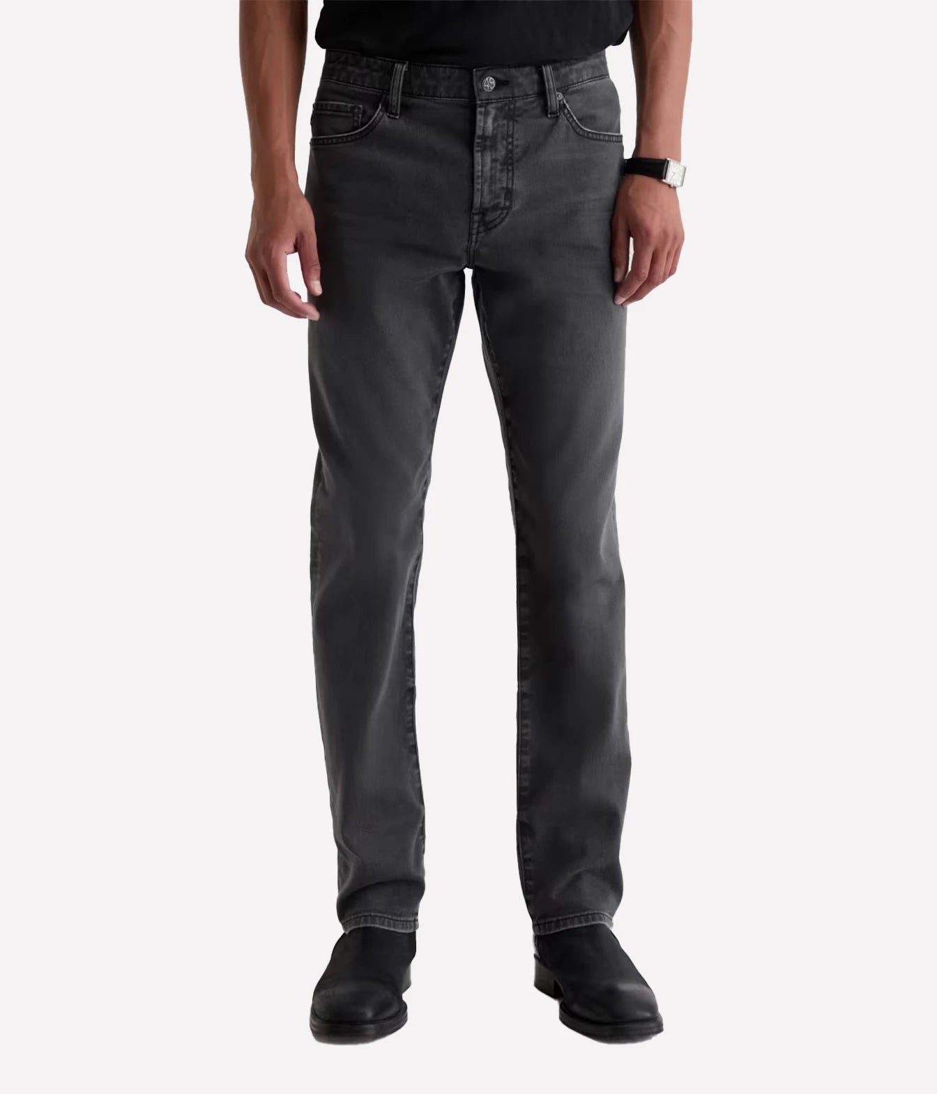 A person wearing slim-fit dark gray washed jeans, a black shirt, and black boots, standing against a light gray studio background.