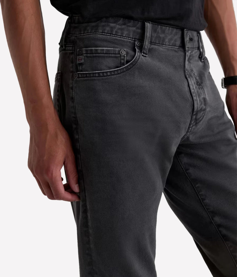 Close-up of a person wearing dark gray washed denim jeans, showing the side pocket, belt loop, waistband, and thigh area against a light gray studio background.