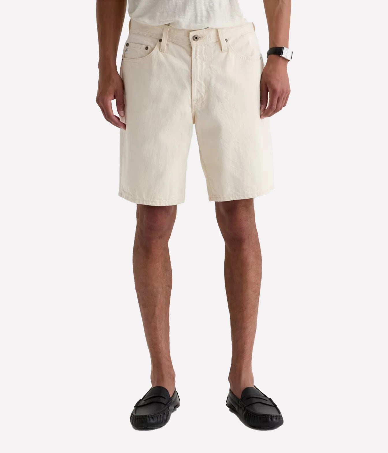 A person wearing off-white denim shorts, a white t-shirt, black loafers, and a black watch, shown from the waist down against a light gray background.