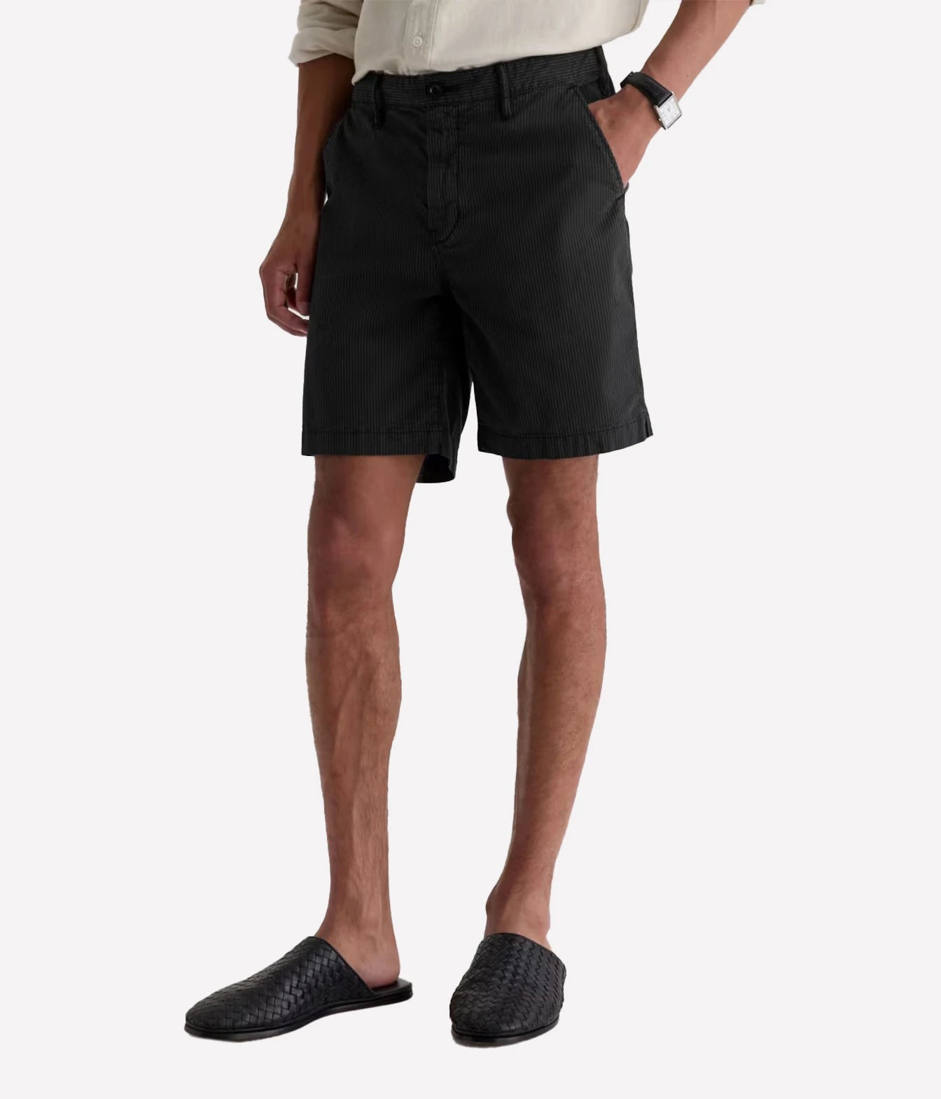 A model wearing black chino shorts, a light beige shirt, and black woven slide sandals, shown from the waist down against a light gray background.