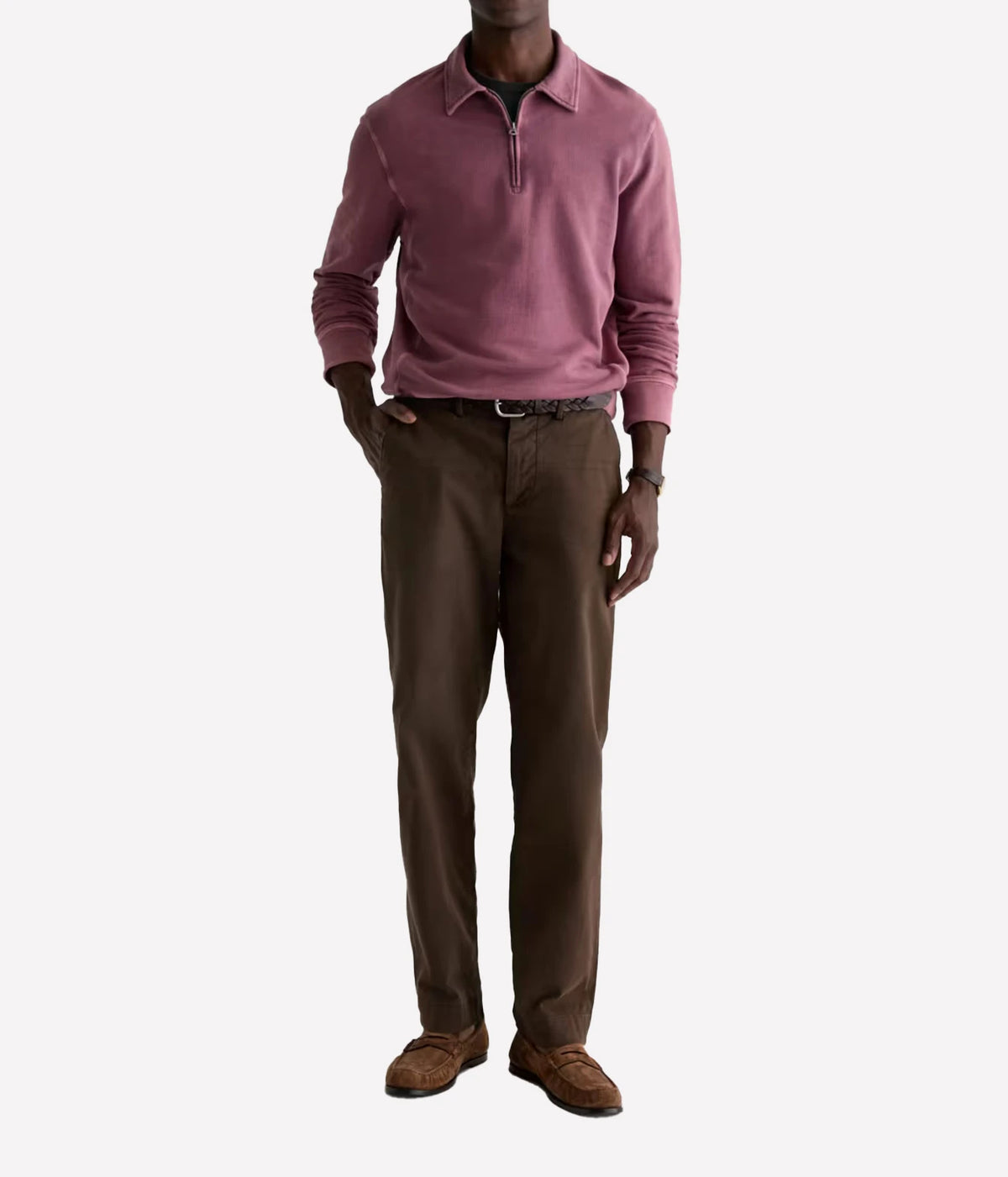 A man wearing a dusty rose quarter-zip long-sleeve polo shirt, brown trousers, and brown suede loafers, standing against a light gray background.