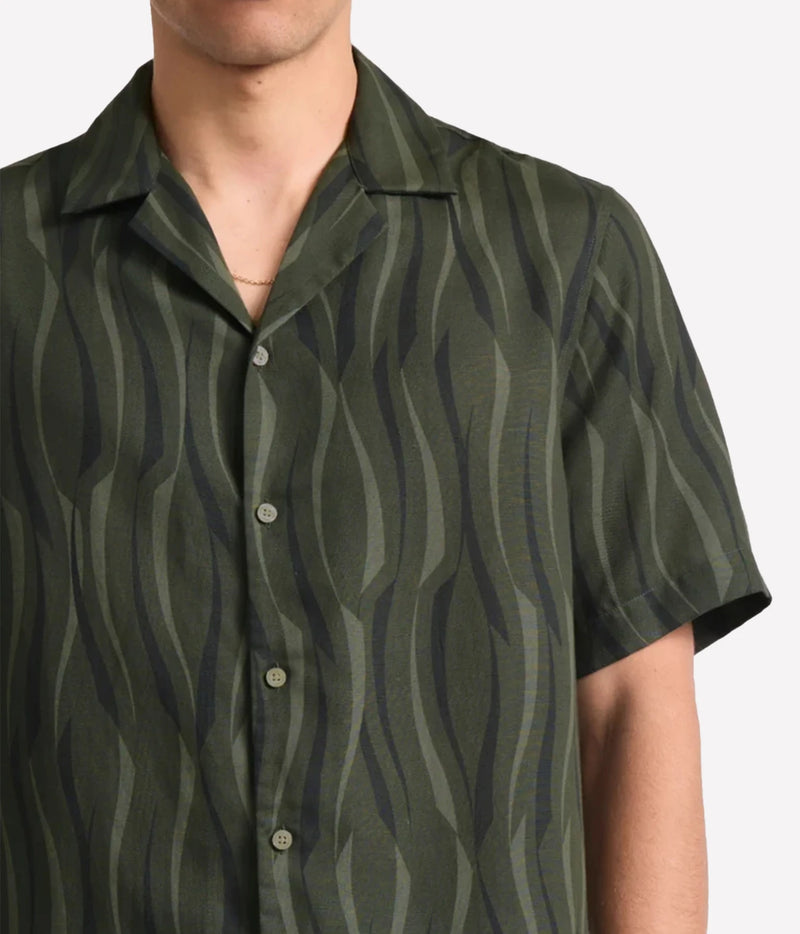 A close-up of a man wearing a Frescobol Carioca Roberto Short Sleeve Linen-Blend Shirt in Cove Green, set against a plain light grey background.