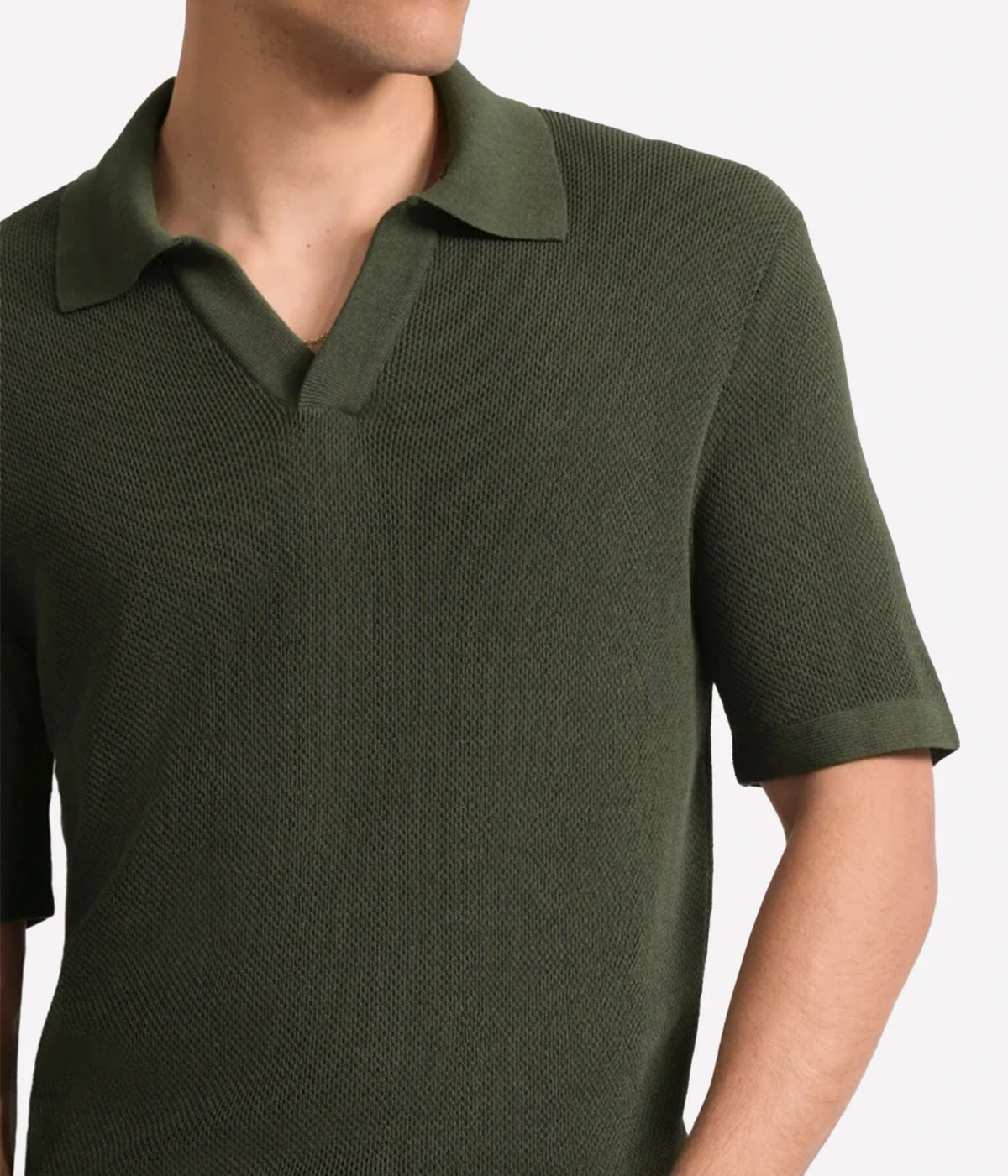 A close-up of a man wearing a Frescobol Carioca Rino Short Sleeve Cotton Polo in Cove Green with a textured knit fabric, set against a plain light grey background.