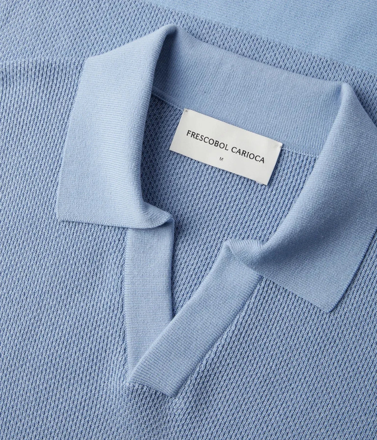 Close-up of a Frescobol Carioca Rino Short Sleeve Cotton Polo in Light Denim Blue with a white brand label reading FRESCOBOL CARIOCA.