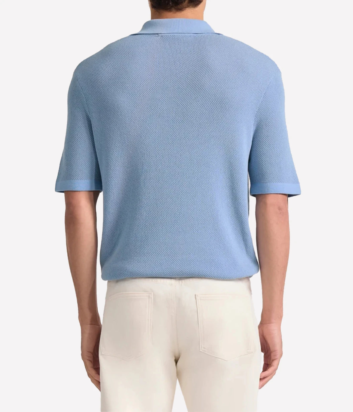 A man viewed from the back wearing a Frescobol Carioca Rino Short Sleeve Cotton Polo in Light Denim Blue and cream-coloured trousers, set against a plain light grey studio background.