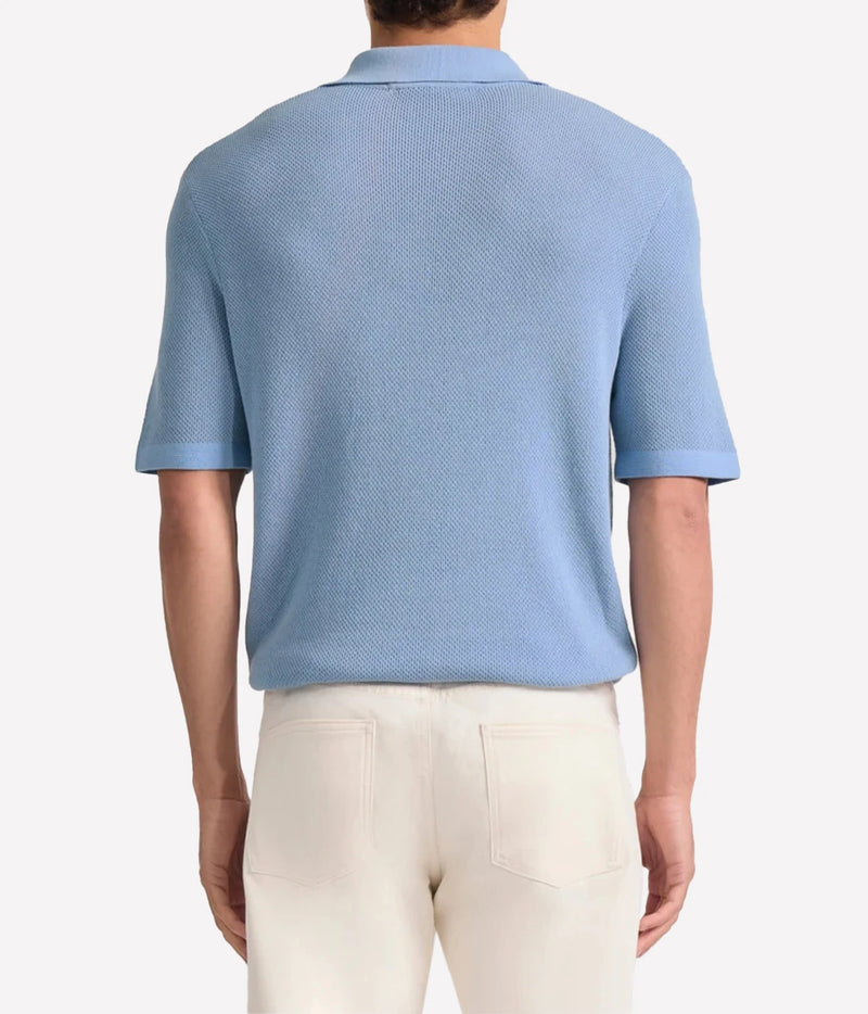 A man viewed from the back wearing a Frescobol Carioca Rino Short Sleeve Cotton Polo in Light Denim Blue and cream-coloured trousers, set against a plain light grey studio background.