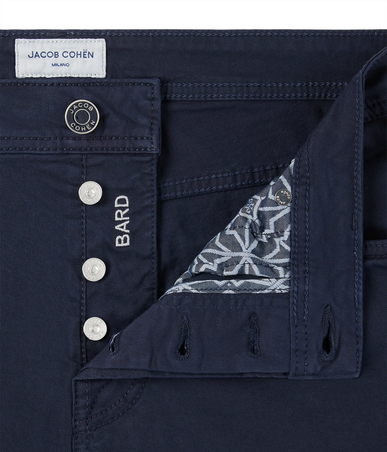 Close-up of dark navy blue jeans by Jacob Cohen, showing the front button closure with silver buttons, a white brand label, and a folded pocket revealing a patterned lining.