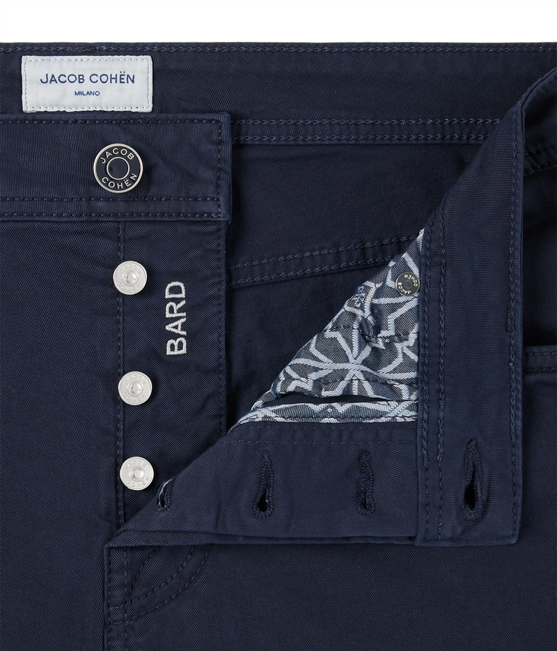 Close-up of dark navy blue jeans by Jacob Cohen, showing the front button closure with silver buttons, a white brand label, and a folded pocket revealing a patterned lining.