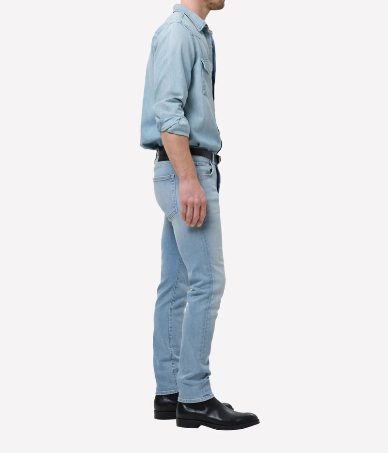 Man wearing Citizens of Humanity London Tapered Slim Perform Jean in Light Wash with a denim shirt, side view