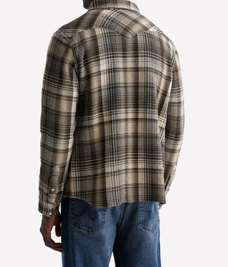 A man wearing a beige, brown, and black plaid flannel shirt, shown from the back, paired with blue jeans against a light gray background.