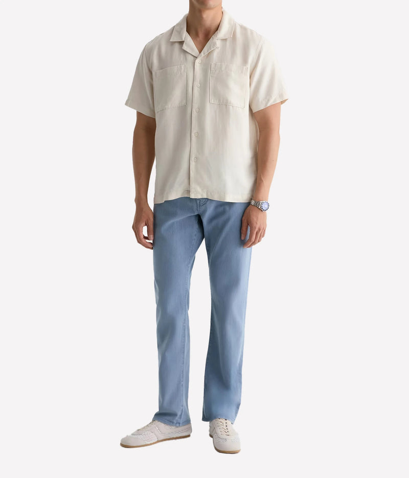 A man modeling a short-sleeve cream-colored camp collar shirt paired with light blue jeans and white sneakers, shown against a plain white background.