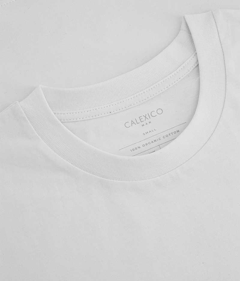 Close-up of a white crewneck t-shirt showing the inner neck label with the brand name CALEXICO MEN.