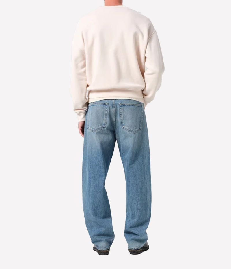 A person shown from the back wearing a cream sweatshirt and light blue relaxed-fit jeans, photographed against a plain light gray studio background.