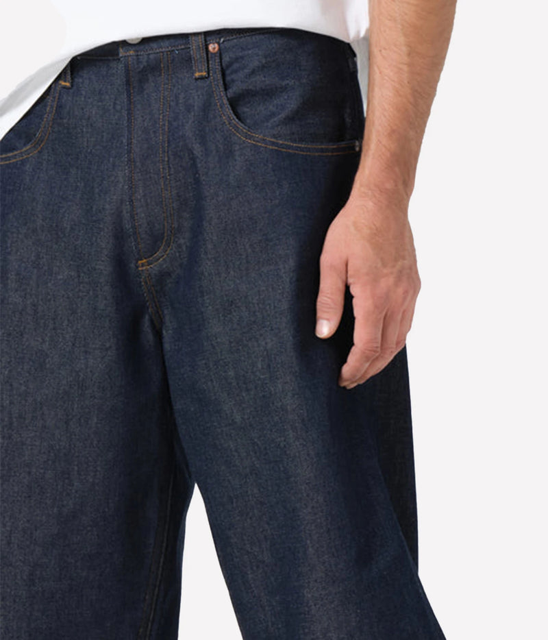 Close-up of a person wearing dark indigo denim jeans with a white shirt partially visible at the top, against a clean white background.