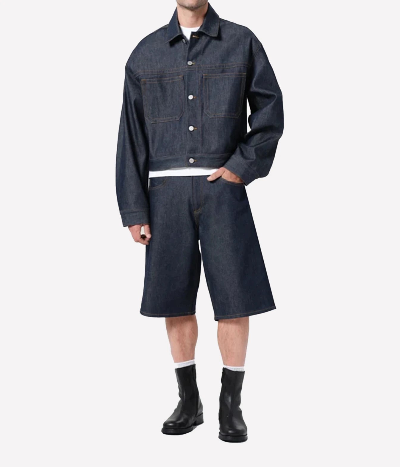 A model wearing a dark indigo denim two-piece set consisting of a cropped button-up jacket and matching shorts, styled with a white t-shirt, white socks, and black boots against a light gray background.