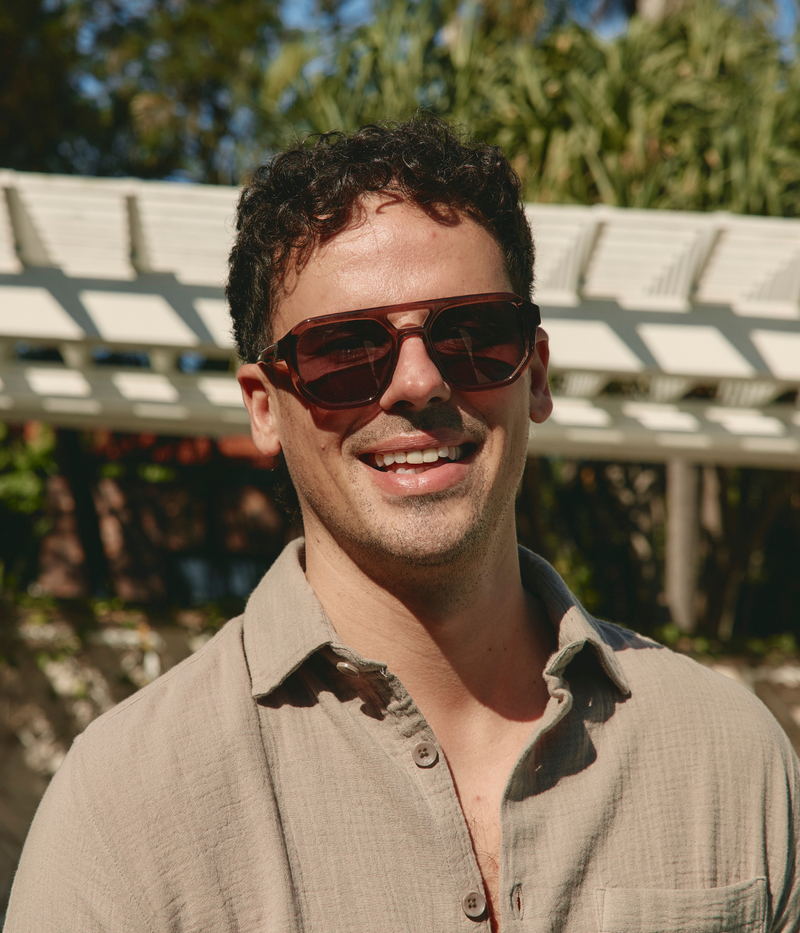 Bold MYKITA sunglasses with matte brown geometric acetate frame, grey lenses, and a cut-out bridge, showcasing signature exposed hinge detailing.