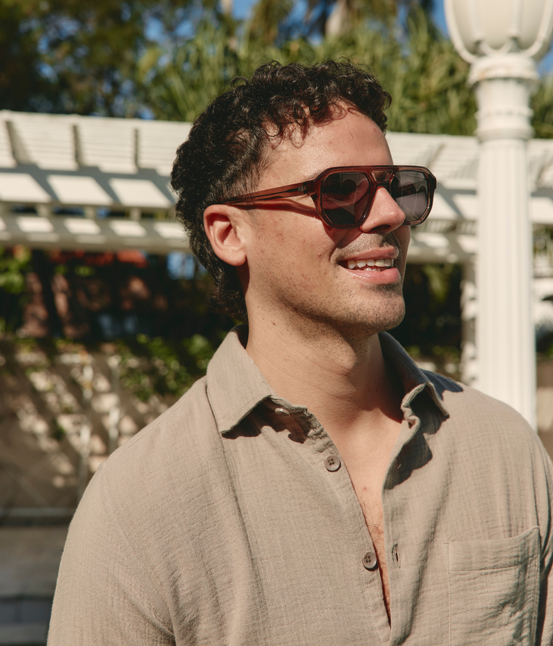 Bold MYKITA sunglasses with matte brown geometric acetate frame, grey lenses, and a cut-out bridge, showcasing signature exposed hinge detailing.