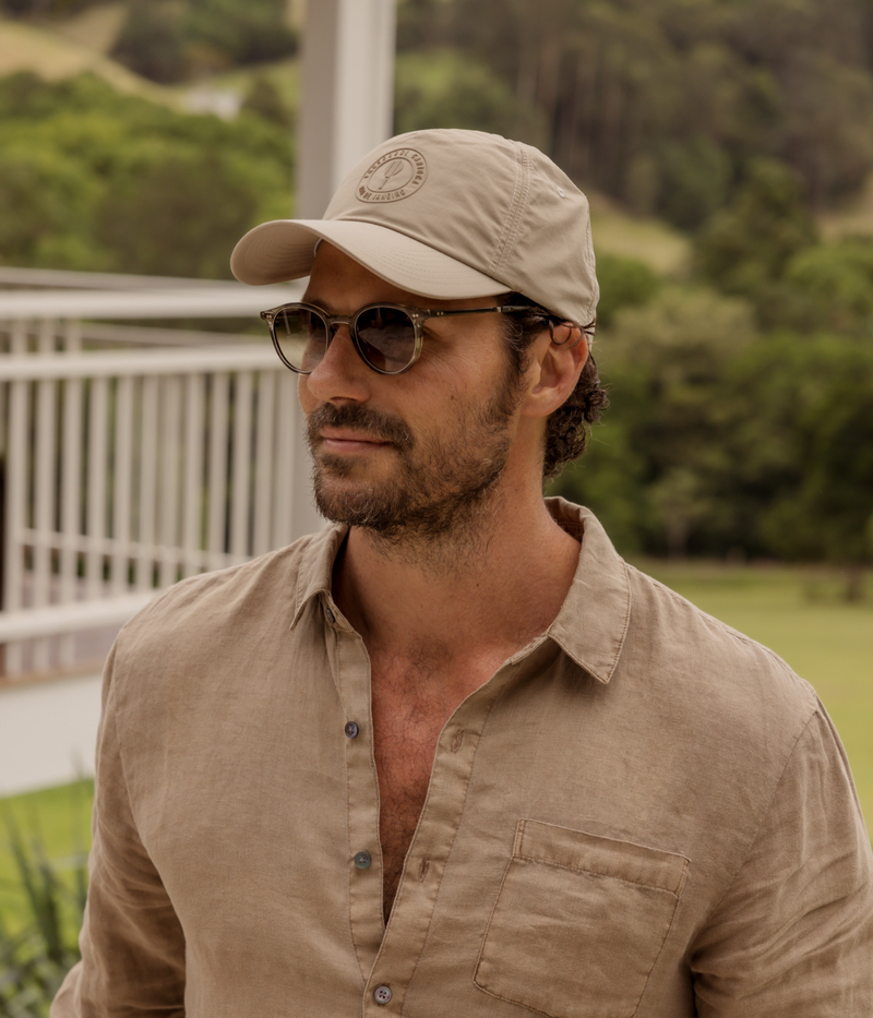 Man wearing a beige cap and sunglasses with a blurred natural background