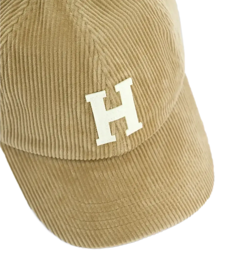 A close-up of a tan corduroy baseball cap featuring a white embroidered letter 'H' on the front, set against a plain white background.