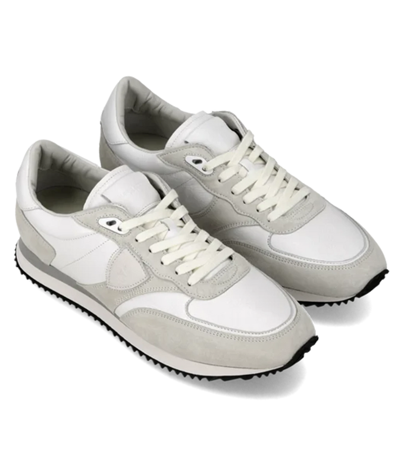 A pair of low-top sneakers in white and light gray suede and leather, featuring white laces and a black treaded outsole, shown on a white background.