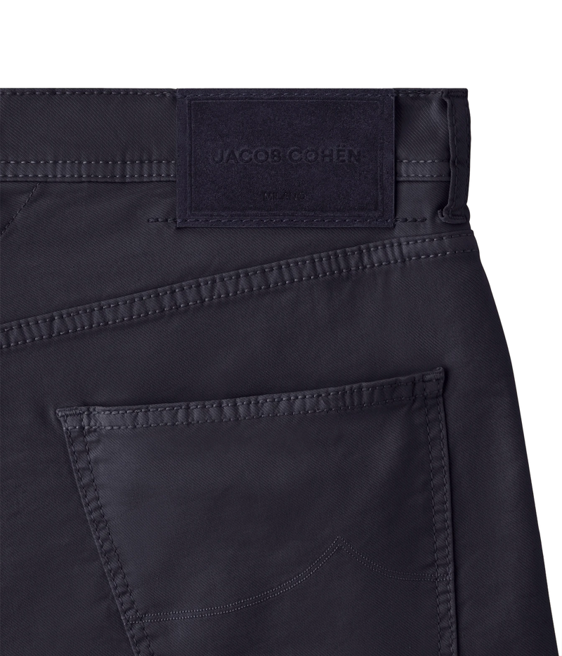 Close-up of the waistband and back pocket of dark navy blue jeans, showing a stitched Jacquob Cohen label at the back waist.