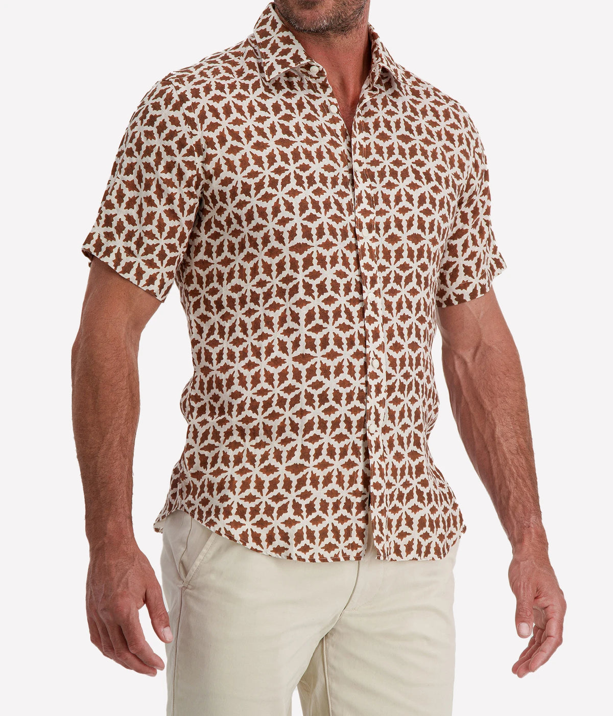 Man wearing Osvaldo Trucchi Linen Short Sleeve Shirt in Brown Geo Star Print with stone shorts, cropped three-quarter view