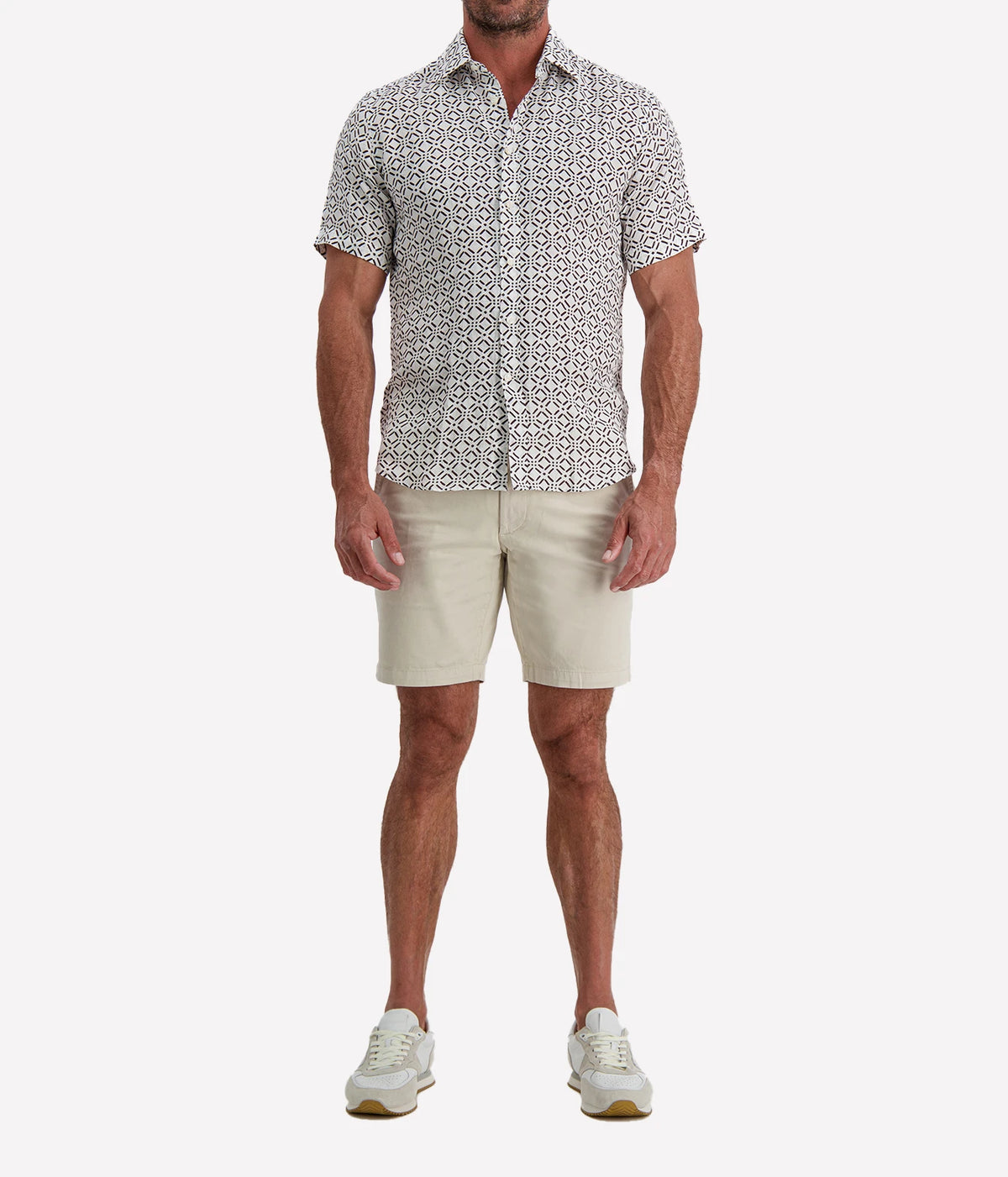 Man wearing Osvaldo Trucchi Linen Short Sleeve Shirt in Brown Geo Diamond Print with stone shorts and white sneakers, full-length front view