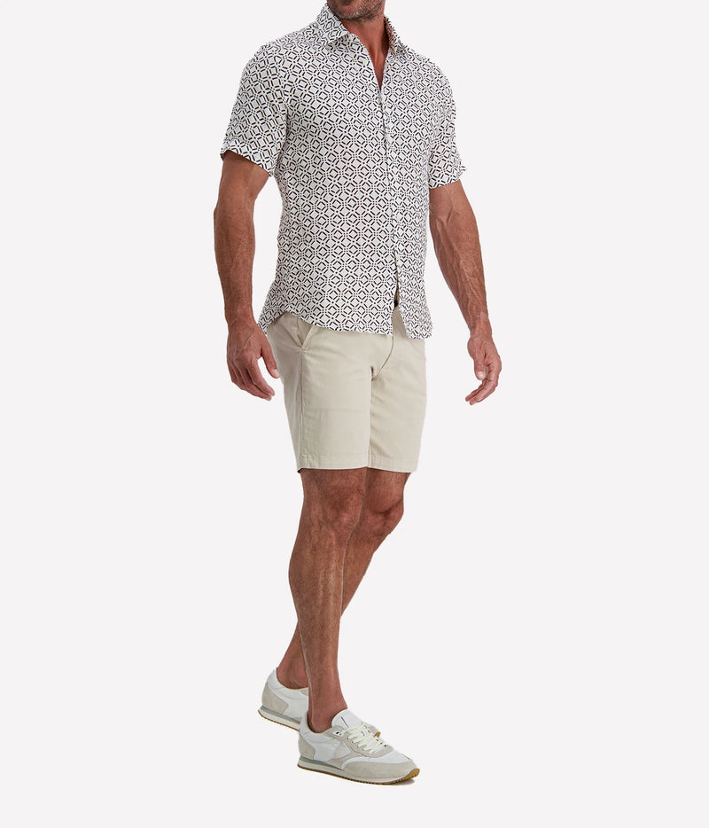 Man wearing Osvaldo Trucchi Linen Short Sleeve Shirt in Brown Geo Diamond Print with stone shorts and white sneakers, three-quarter view
