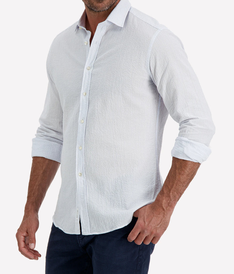 Man wearing Ingram Slim Fit Shirt in Seersucker Blue & White Stripe with indigo jeans, cropped angled front view with hand in pocket