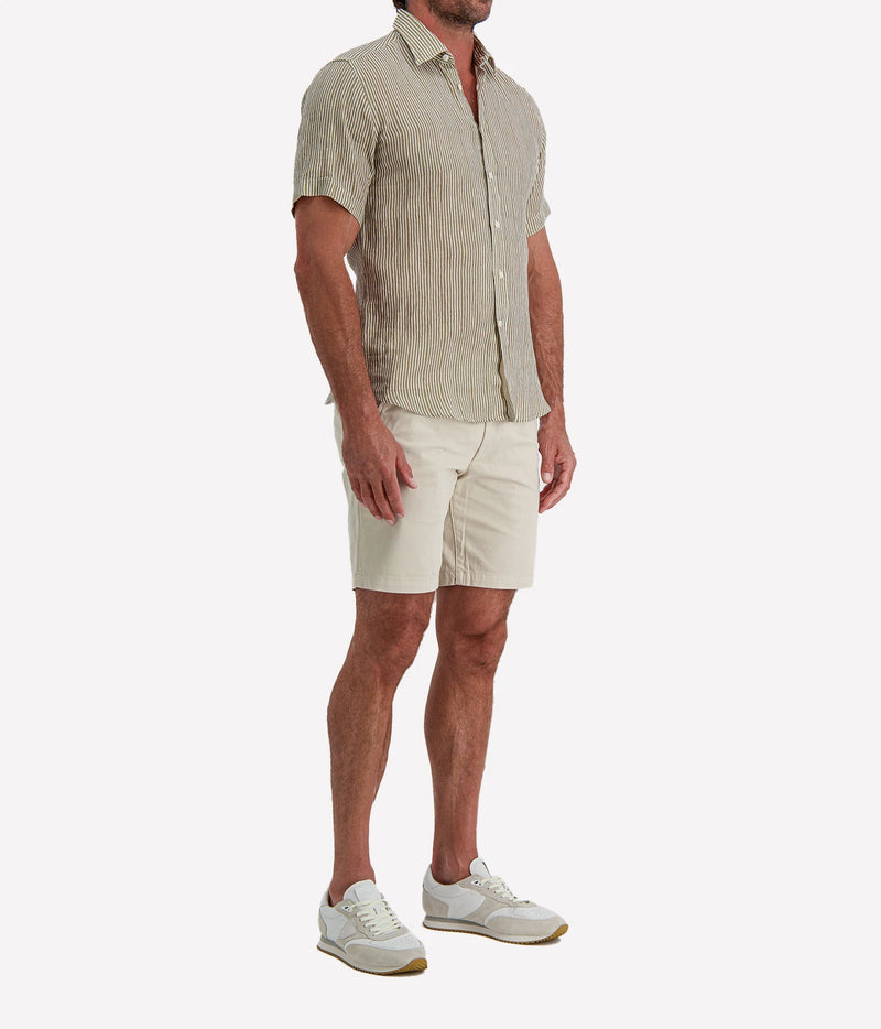 Man wearing Osvaldo Trucchi Linen Short Sleeve Shirt in Olive and White Stripe with stone shorts and white sneakers, side view