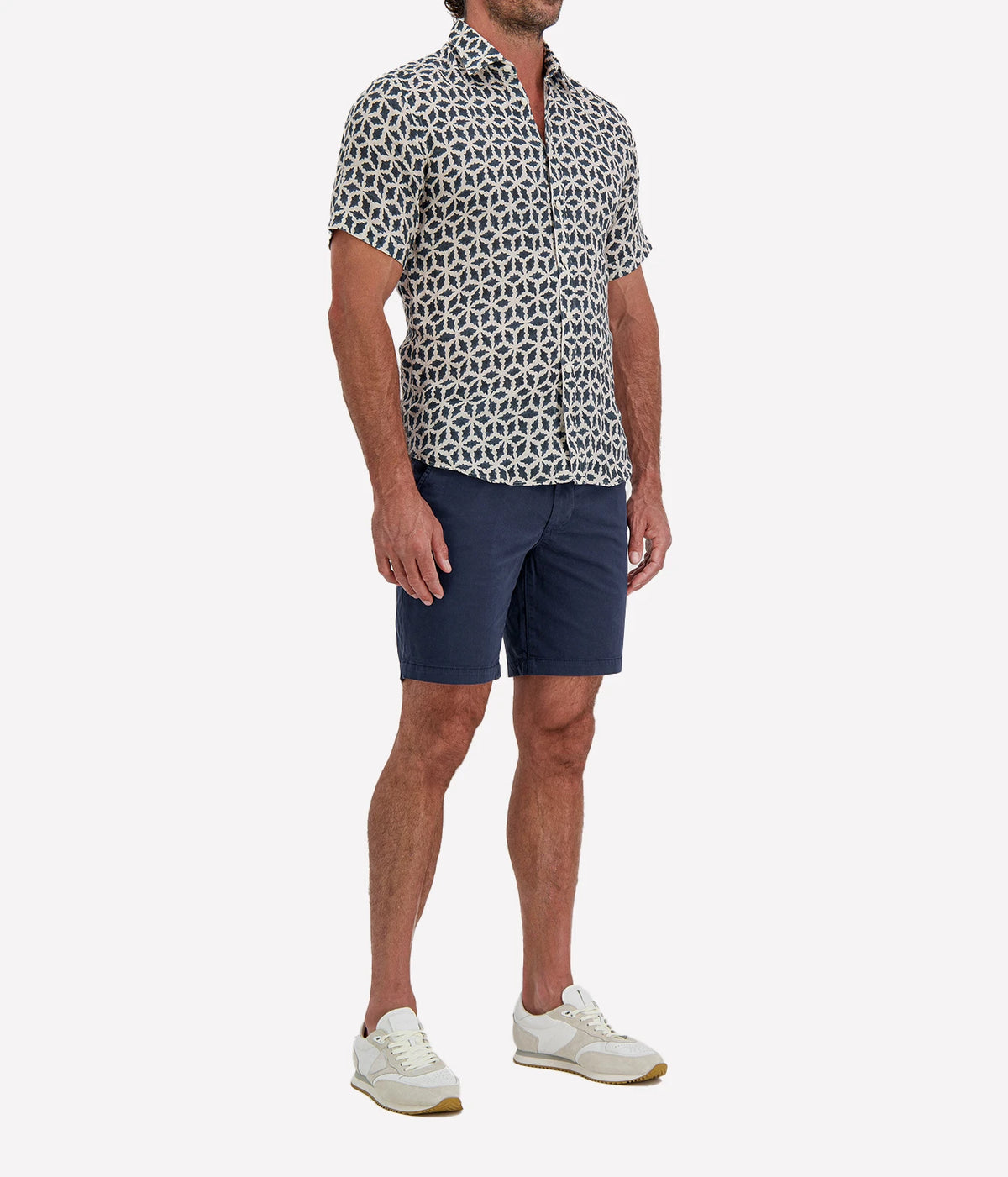 Man wearing Osvaldo Trucchi Linen Short Sleeve Shirt in Navy Geo Star Print with navy shorts and white sneakers, three-quarter view