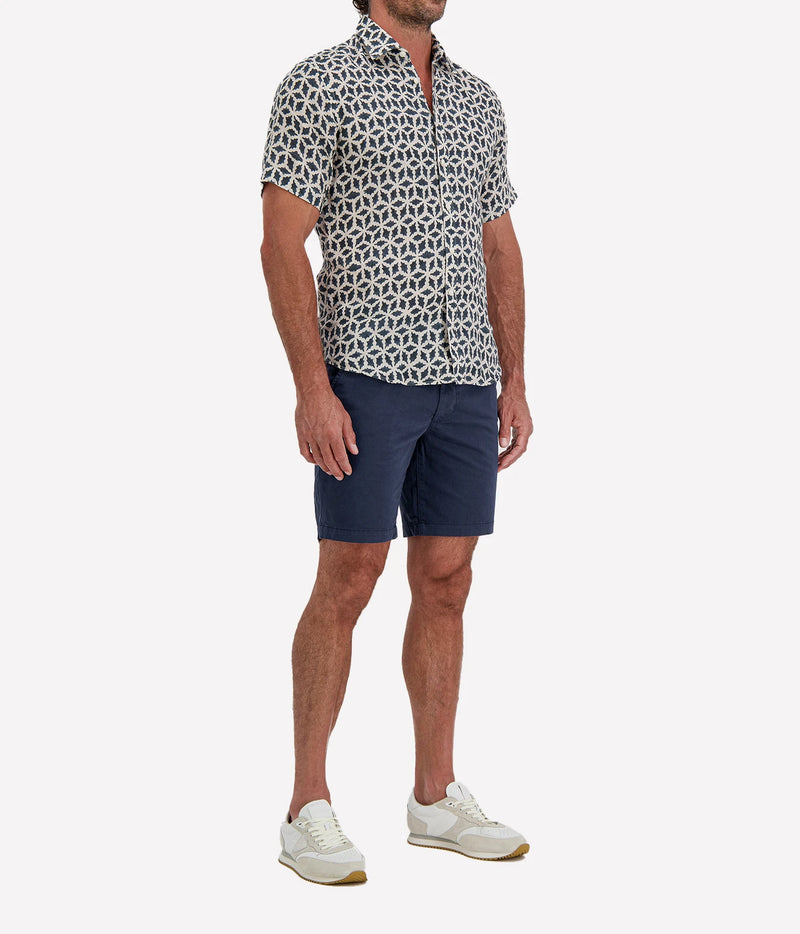 Man wearing Osvaldo Trucchi Linen Short Sleeve Shirt in Navy Geo Star Print with navy shorts and white sneakers, three-quarter view