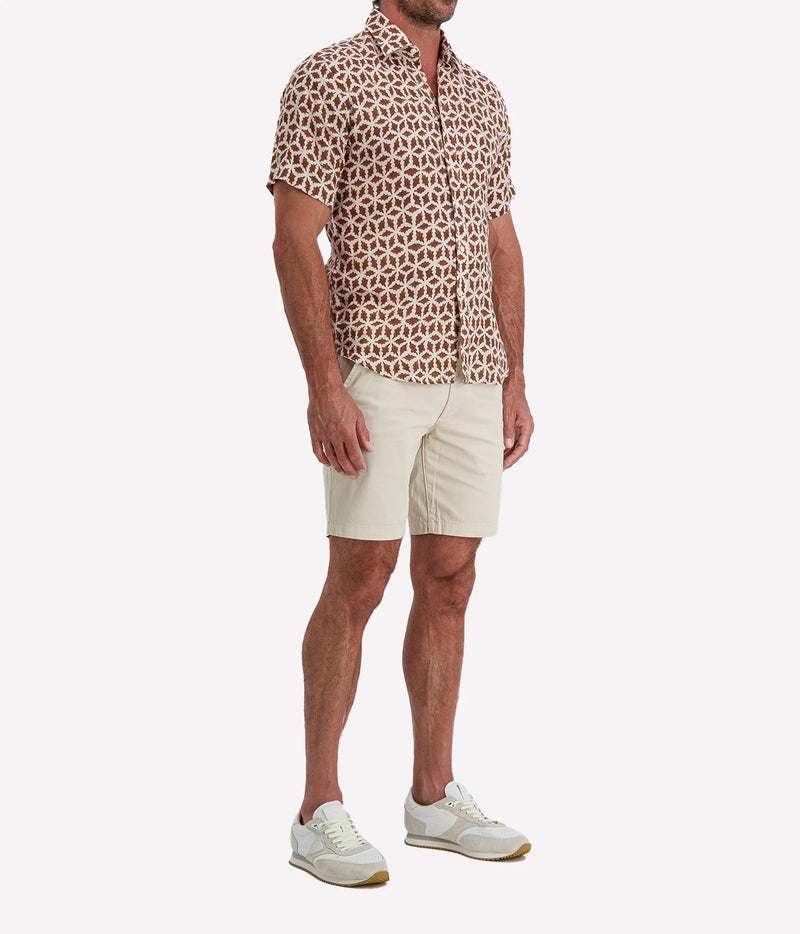 Man wearing Osvaldo Trucchi Linen Short Sleeve Shirt in Brown Geo Star Print with stone shorts and white sneakers, side view