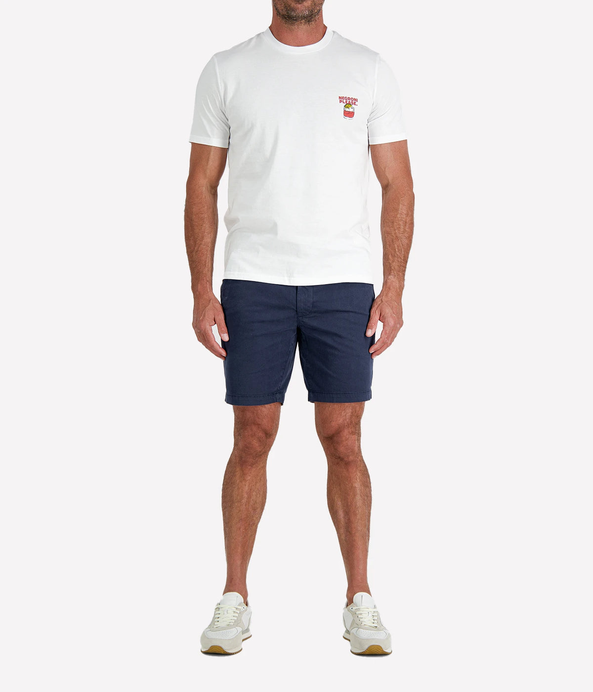 Man wearing The Refined Spirit Negroni Please Tee in White with navy shorts and white sneakers, full-length front view