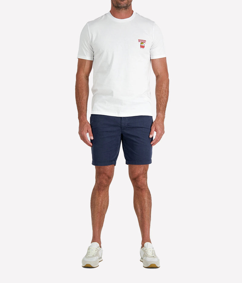 Man wearing The Refined Spirit Negroni Please Tee in White with navy shorts and white sneakers, full-length front view