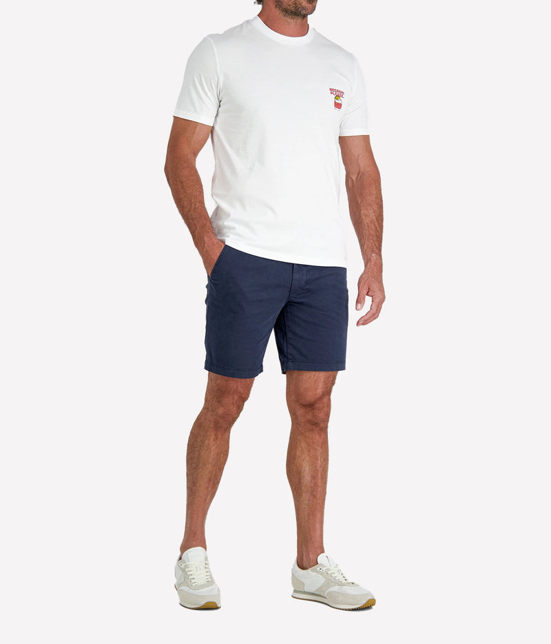 Man wearing The Refined Spirit Negroni Please Tee in White with navy shorts and white sneakers, three-quarter view