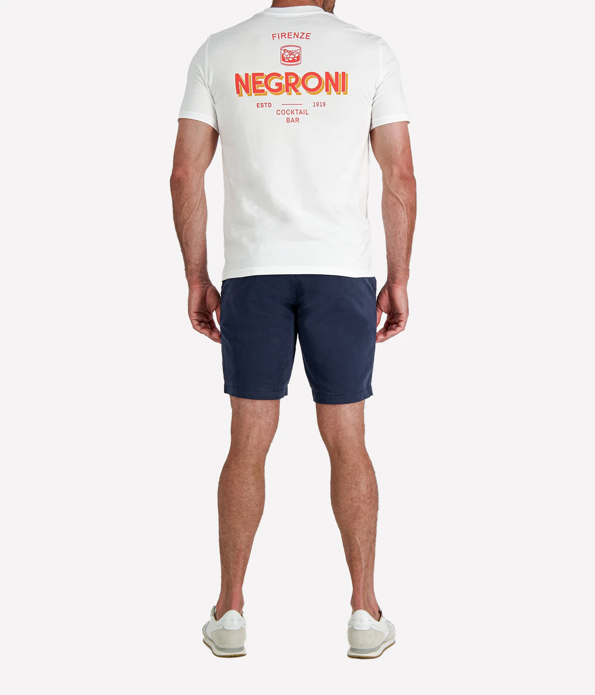 Back view of man wearing The Refined Spirit Negroni Cocktail Bar Tee in White with navy shorts and white sneakers