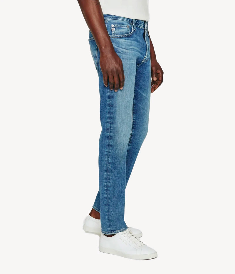 Side profile of the Dylan slim skinny jeans in medium indigo wash, highlighting the tapered fit from thigh to ankle. The subtle fading and whiskering add character while maintaining a clean, contemporary silhouette.